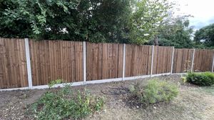 A long run of wooden fence, using concrete posts and kick-boards.