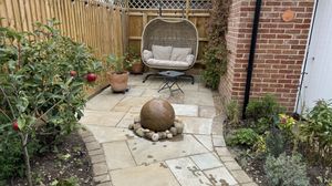 A wooden fenced and paved hidden seating area garden with built in water feature.